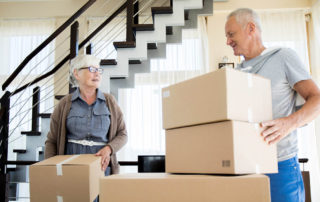 Portrait of happy senior couple packing cardboard boxes while moving to new house