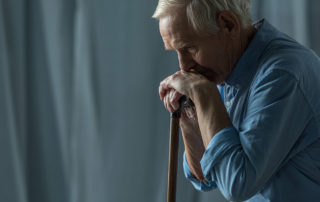 Senior sad man leans on a cane while sitting on sofa