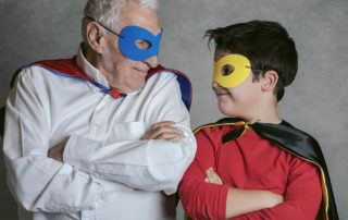 Grandfather With Grandson dressed as a superhero on gray background